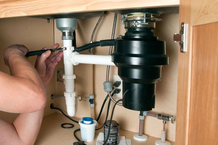 Plumber installing a garbage disposal beneath a kitchen sink in Springfield